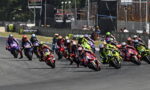 Group of motorcycle racers lean into a curve on a race track, colorful bikes and gear creating a vivid sprint to the turn.