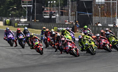 Group of motorcycle racers lean into a curve on a race track, colorful bikes and gear creating a vivid sprint to the turn.