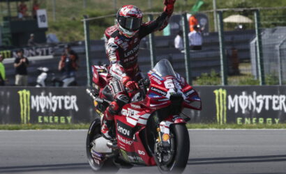 Racing rider on a red Ducati Lenovo bike raises a fist in celebration on a track, with Monster Energy banners in the background.