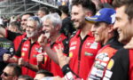 Group of Ducati racing team members in red shirts celebrate with raised fists at a motorsport event.