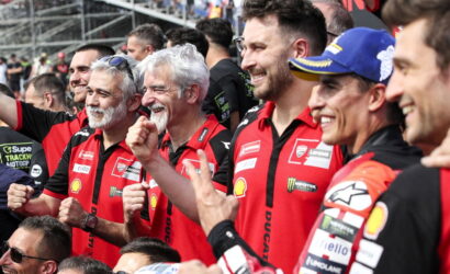 Group of Ducati racing team members in red shirts celebrate with raised fists at a motorsport event.