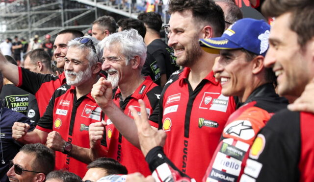 Group of Ducati racing team members in red shirts celebrate with raised fists at a motorsport event.