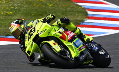 Professional motorcycle racer in a neon-yellow suit riding a bright yellow race bike, leaning into a corner on a racetrack.