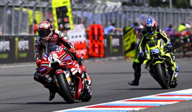 Racing motorcycles on a track; a red-and-white bike leads, rider leaning into a turn in red race gear, another yellow-and-black bike nearby.