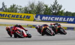 Four motorcycle racers lean into a turn on a race track, with a Michelin banner in the background.