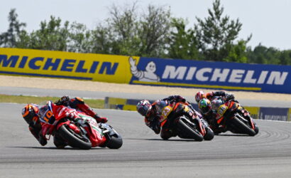 Four motorcycle racers lean into a turn on a race track, with a Michelin banner in the background.