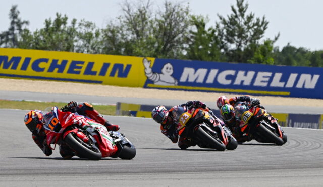 Four motorcycle racers lean into a turn on a race track, with a Michelin banner in the background.