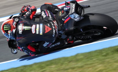 Motorcycle racer in black and red leathers leans into a turn on a blue-edged race track.