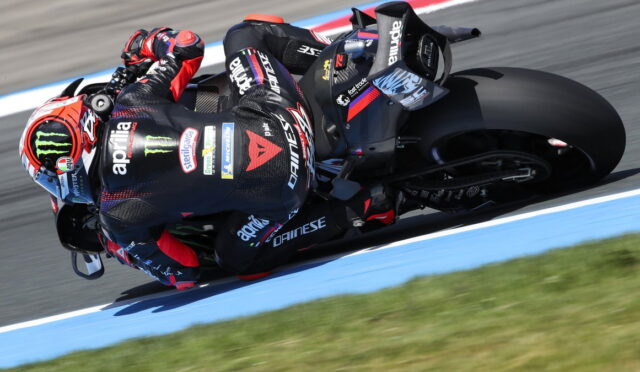 Motorcycle racer in black and red leathers leans into a turn on a blue-edged race track.