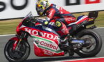 A red, white, and blue Honda racing bike with Castrol livery speeding on a track, rider in matching suit and helmet leaning into a turn.