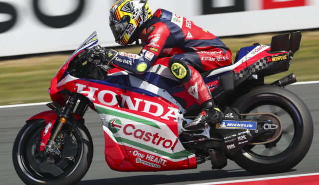 A red, white, and blue Honda racing bike with Castrol livery speeding on a track, rider in matching suit and helmet leaning into a turn.