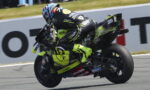 Motorcycle racer in a neon-yellow suit leans into a turn on a race track, bike number 25.