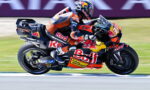 MotoGP rider in Red Bull KTM livery leaning into a high-speed corner on a race track with motion blur in the background.