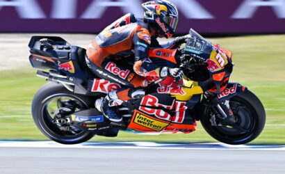 MotoGP rider in Red Bull KTM livery leaning into a high-speed corner on a race track with motion blur in the background.