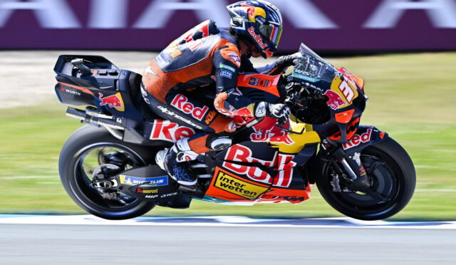 MotoGP rider in Red Bull KTM livery leaning into a high-speed corner on a race track with motion blur in the background.