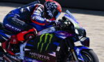Motorcycle racer in blue and red leathers leaning into a turn on a Yamaha Monster Energy bike, racing on track.