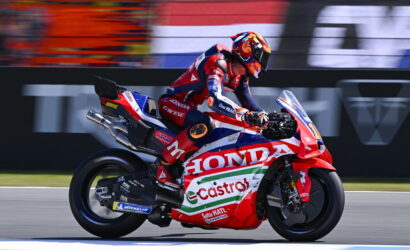 MotoGP rider in red-blue leathers on a Honda Castrol race bike speeding along a racetrack with a blurred background.