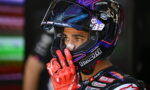 Close-up of a motorcycle racer in a colorful helmet with the number 89, wearing red racing gloves and looking intently ahead.