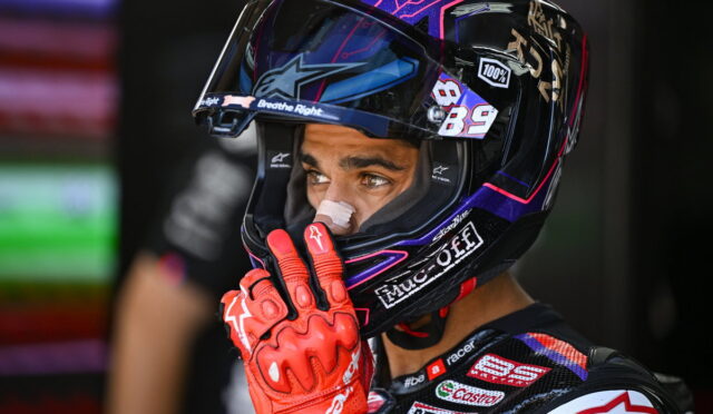 Close-up of a motorcycle racer in a colorful helmet with the number 89, wearing red racing gloves and looking intently ahead.