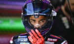 Motocross racer in a purple helmet with red gloves, hand near the face shield, looking ahead.