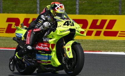 Racer on a neon-yellow sport bike leaning into a turn on a race track, DHL banners in the background.