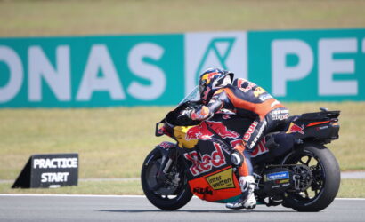 MotoGP rider in full leathers leaning into a turn on a race bike with Red Bull livery.