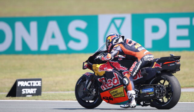 MotoGP rider in full leathers leaning into a turn on a race bike with Red Bull livery.