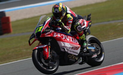 Moto racing rider on a red Honda sport bike, leaning into a corner on a racetrack.