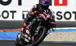 MotoGP rider leaning into a left-hand turn on a black racing bike with sponsor decals on the suit and bike