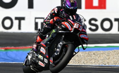 MotoGP rider leaning into a left-hand turn on a black racing bike with sponsor decals on the suit and bike