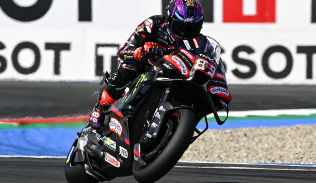 MotoGP rider leaning into a left-hand turn on a black racing bike with sponsor decals on the suit and bike