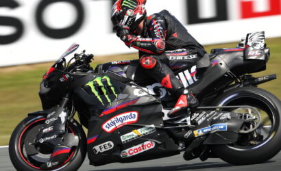 MotoGP rider in black and red gear leans into a turn on a sponsor-covered racing bike with Monster Energy and Castrol logos.