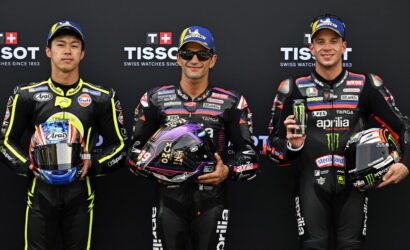 Three motorcycle racers in full leathers stand side by side holding helmets, posing against a Tissot backdrop.