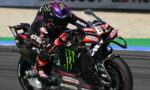 Motorcycle racer leaning into a turn on a black race bike with Monster Energy logos and sponsor decals.