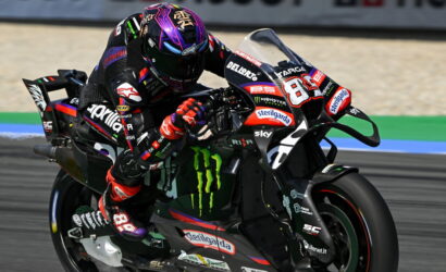 Motorcycle racer leaning into a turn on a black race bike with Monster Energy logos and sponsor decals.