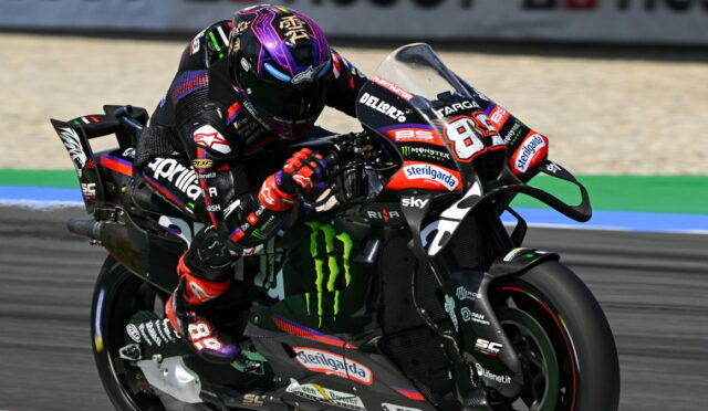Motorcycle racer leaning into a turn on a black race bike with Monster Energy logos and sponsor decals.