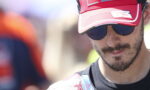 Man wearing a red cap and dark sunglasses, partial face visible outdoors, slight smile on lips.