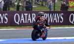 MotoGP rider in Red Bull KTM gear exits a corner on a race track; blue runoff area and spectators behind a fence with Qatar Airways advertising