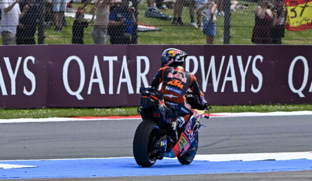 MotoGP rider in Red Bull KTM gear exits a corner on a race track; blue runoff area and spectators behind a fence with Qatar Airways advertising
