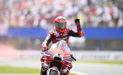 Racer on a red Lenovo motorcycle on the track, helmeted rider waving to the cheering crowd