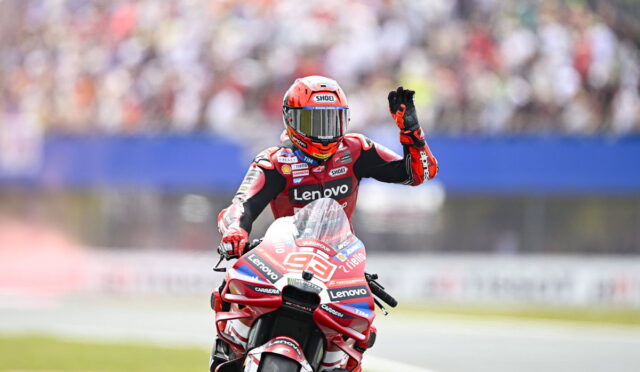 Racer on a red Lenovo motorcycle on the track, helmeted rider waving to the cheering crowd