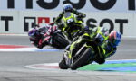 Riders on sport motorcycles leaning into a sharp turn on a race track in a high-speed race scene.