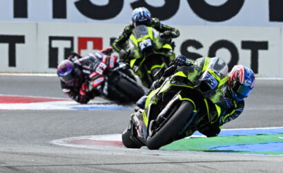 Riders on sport motorcycles leaning into a sharp turn on a race track in a high-speed race scene.