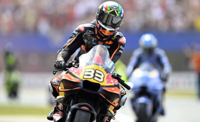 Motorcycle racer wearing a black and orange suit on an orange KTM bike with number 33, Red Bull livery, leaning into a turn.