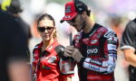 MotoGP rider in red and black racing suit and cap stands with a female team member in a red polo, both looking focused.