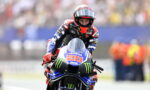 MotoGP rider on a Yamaha bike, number 20, in a red-helmeted racing suit leaning into a turn on the track.
