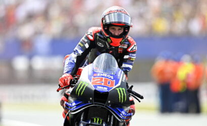 MotoGP rider on a Yamaha bike, number 20, in a red-helmeted racing suit leaning into a turn on the track.