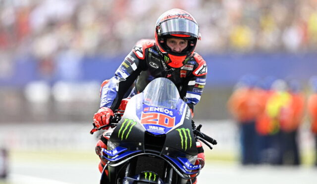 MotoGP rider on a Yamaha bike, number 20, in a red-helmeted racing suit leaning into a turn on the track.