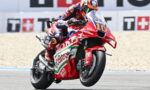 Moto racer in red-blue suit leaning into a turn on a red Honda bike with Costa branding, number 10 visible.