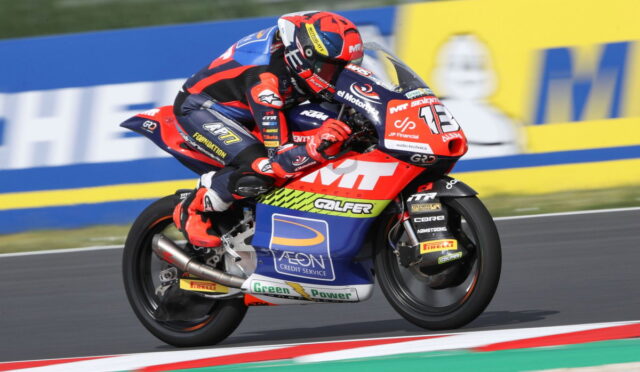 Motorcycle racer in red-blue suit leaning into a turn on a race track with a sponsor-labeled bike in red, blue, and white.